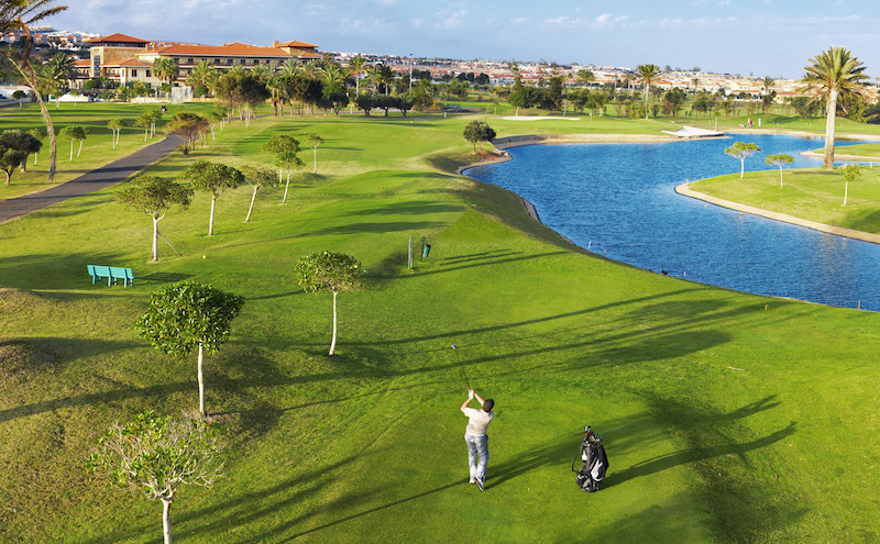 Golfer playing a fairway shot on a water lined hole, with the Elba Palace Hotel in the background