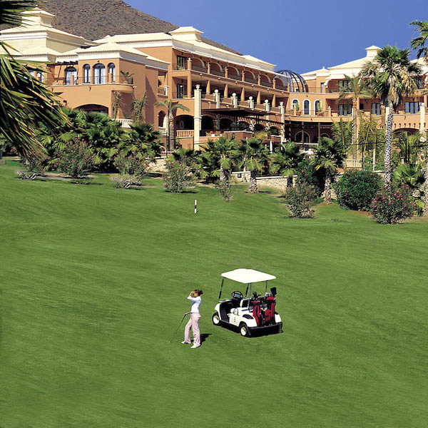 Golfers with buggy on Golf Las Americas with Hotel Las Madrigueras in background